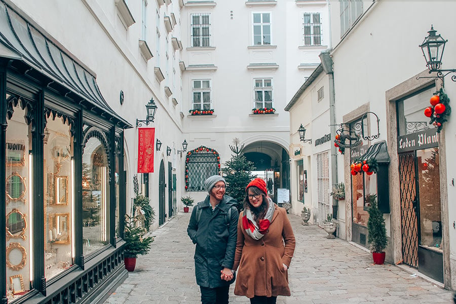 Couple wearing winter coats in a holiday-decorated alley in Vienna, Austria.