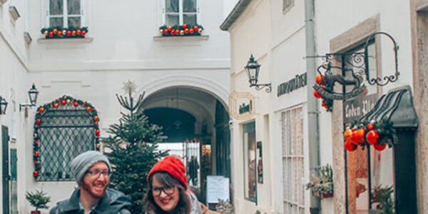 Lia and Jeremy hand in hand in Christmassy decorated alley in Vienna, Austria.