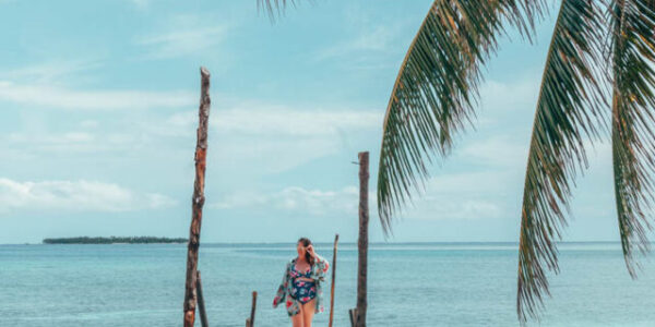 Curvy girl on a dock in front of a bright blue sea with a palm tree in one corner.