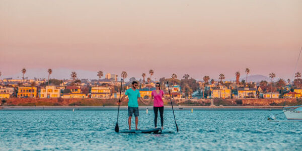 Couple paddle boarding together on the bay during sunset in San Diego, CA.