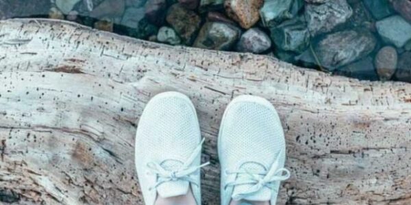 Lia in Allbirds shoes while standing on a log with rocks below
