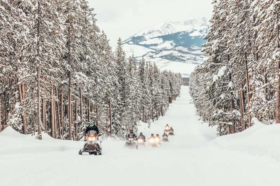 Snowmobiles driving on a snowy road in the forest with the Grand Tetons in the background in Yellowstone National Park