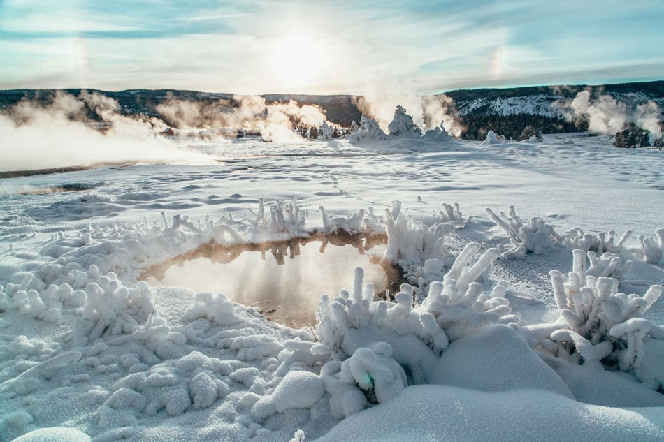 Upper Geyser Basin with steam coming up surrounded by snow in Yellowstone National Park